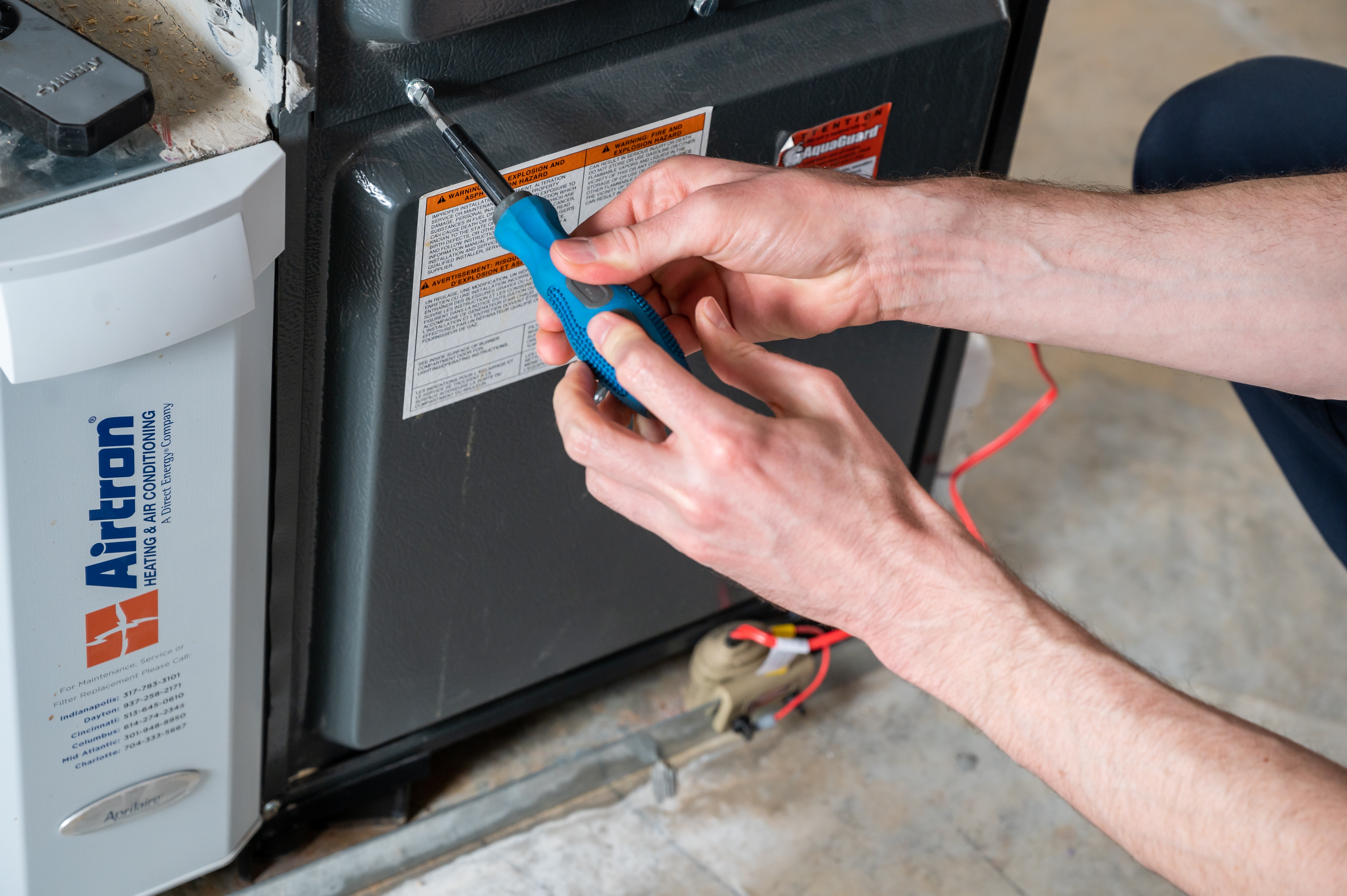 Close-up of an HVAC technician servicing a furnace with a screwdriver